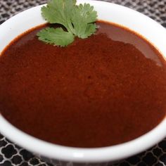 a white bowl filled with red sauce and garnished with cilantro leaves