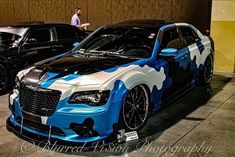 two cars parked next to each other in a parking lot with one car painted blue and the other white