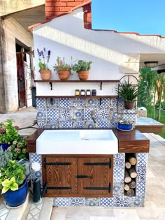 an outdoor kitchen with blue and white tiles on the outside wall, potted plants in pots