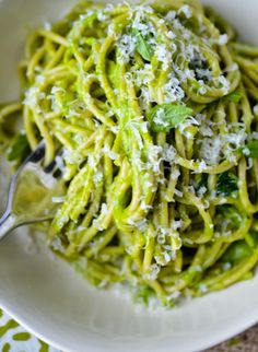 a white bowl filled with green pasta and parmesan cheese