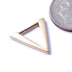 a small triangle shaped pin sitting next to a penny