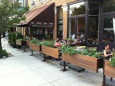 people sitting at tables in front of a restaurant with plants growing out of the windows