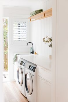 a washer and dryer in a white laundry room with wood flooring on the side