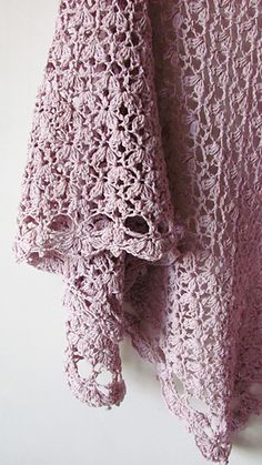 a pink crocheted shawl hanging on a white wall