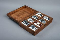 an open wooden watch box with twelve watches in it's compartments on a grey background