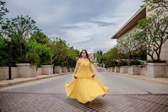 a woman in a yellow dress is walking down the street with her arms raised up