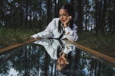 a woman leaning on the edge of a pool with trees in the background and water reflecting her face