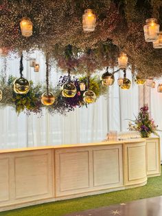 an elegant reception setup with hanging lights and flowers on the wall, along with greenery