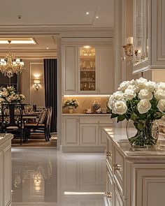 an elegant kitchen with white cabinets and marble counter tops, chandeliers and vases filled with flowers