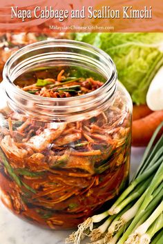 a glass jar filled with food sitting on top of a counter next to green onions and carrots