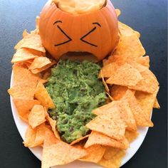 a white plate topped with chips and a pumpkin shaped bowl filled with guacamole