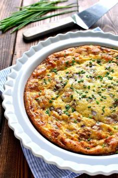 a quiche in a white dish on top of a wooden table next to a knife and fork