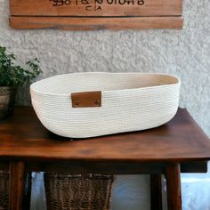 a white basket sitting on top of a wooden table next to a potted plant