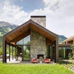 a modern house with a stone fireplace in the front yard and mountains in the background