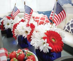 red, white and blue flowers in vases with strawberries on the table next to them