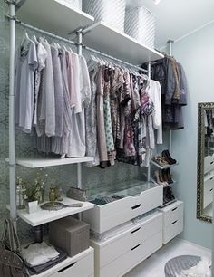 an organized closet with white drawers and clothes hanging on the wall, along with mirror