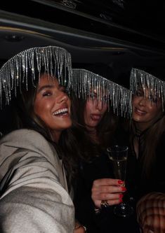 three women wearing tinsel on their head and holding a wine glass in front of them