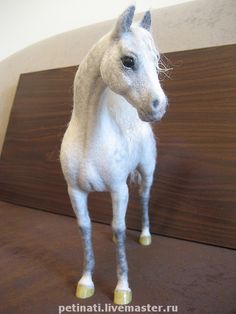 a small white horse standing on top of a wooden floor next to a brown wall