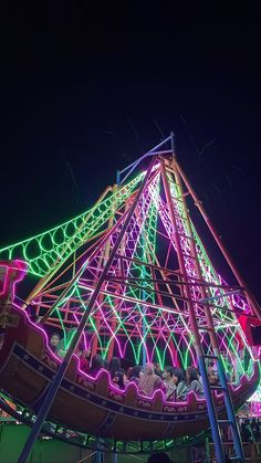 an amusement park ride lit up at night with colorful lights on the top and sides