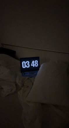 an alarm clock sitting on top of a bed next to pillows and blankets in a dark room