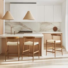 two wooden stools sit in front of an island with marble counter tops and pendant lights