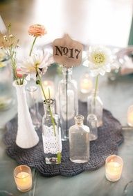 a table topped with vases filled with flowers and candles next to small glass bottles