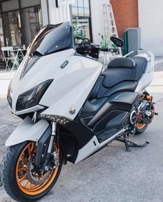 a white and black motorcycle parked in front of a building with orange rims on it