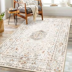 a white rug with an ornate design on the floor in front of a chair and window