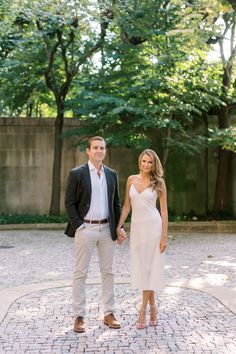 a man and woman standing next to each other on a brick walkway with trees in the background