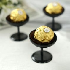 three chocolate covered desserts sitting on top of black pedestals in front of a white tablecloth