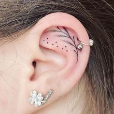 a woman's ear has a small flower and leaf tattoo on the left side