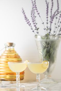 two glasses filled with yellow liquid sitting on top of a table next to a vase