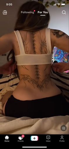 the back of a woman with tattoos on her body sitting on top of a bed