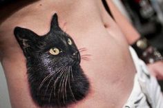 a black cat tattoo on the side of a woman's stomach, with yellow eyes