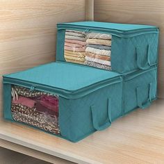 two blue storage bins on top of a wooden shelf filled with folded clothes and blankets