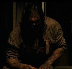 a man with long hair and beard wearing an apron is cutting something on a table