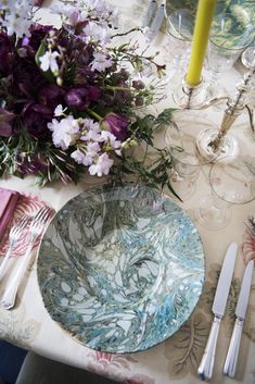 the table is set with purple and white flowers, silverware, and wine glasses