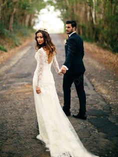 a bride and groom holding hands while standing on the road in front of some trees