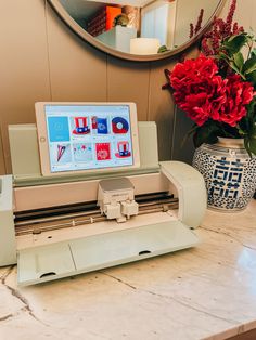 a laptop computer sitting on top of a machine next to a vase with red flowers