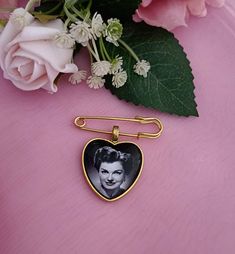 a close up of a heart shaped brooch on a pink surface with flowers in the background