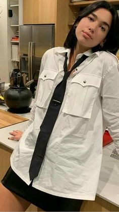 a woman standing in a kitchen wearing a shirt and tie with her hands on her hips