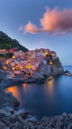 the village is lit up at night on top of a cliff overlooking the water and rocks