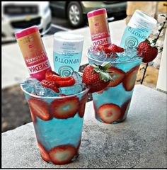 three glasses filled with ice and strawberries on top of a cement table next to a car