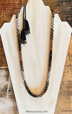 the beaded necklace is on display in front of a wooden stand with white and black beads