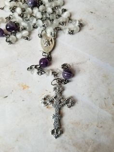 This is a gorgeous five-decade Catholic rosary. These pieces were made using gunmetal and silver findings, centers, and crucifixes. The decade beads are 6mm ivory cat eye glass beads. The Father beads are 8mm chevron amethyst. The rosary chain is hand wired using gunmetal eye pins. This is handmade chain, not store-bought. The sections are connected with small bits of gunmetal chain. The jump rings, centers, and crucifixes are dark silver color. They go well with the gunmetal chain. The center i Handmade Silver Rosary With Crucifix, Handmade Silver Rosary For Healing, Silver Spiritual Rosary For Healing, Types Of Prayer, Decade Rosary, Chakra Colors, Sacred Heart Of Jesus, Handmade Chain, Chevron Amethyst