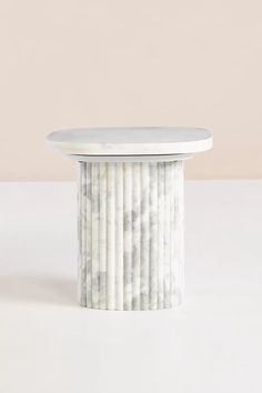 a white marble table sitting on top of a white floor next to a pink wall