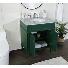 a white toilet sitting next to a green cabinet in a bathroom under a round mirror