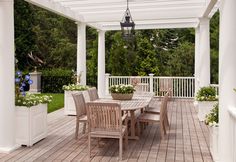 an outdoor dining table and chairs on a wooden deck with white walls and ceilinging