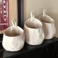 three white storage bags sitting on top of a black shelf next to a framed painting