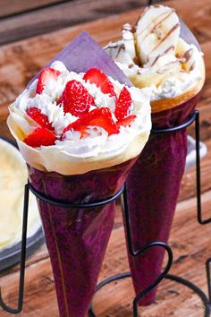 two dessert cones with strawberries and whipped cream on them sitting on a wooden table